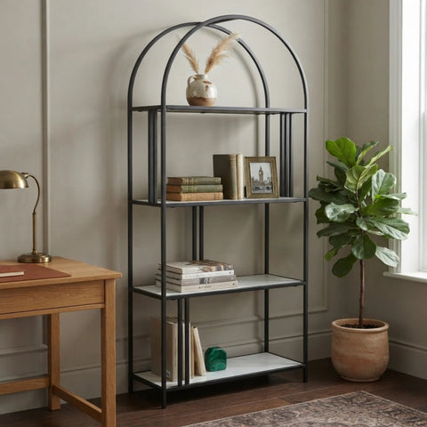 A tall black metal shelving unit with an arched top frame and four open shelves, styled in a home office setting next to a wooden desk and a potted fiddle-leaf fig plant.