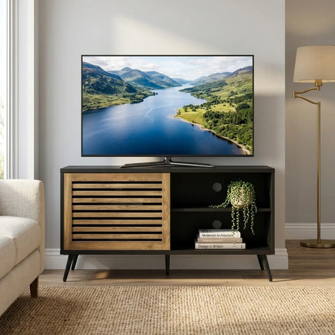 TV on a wooden stand displaying a mountainous landscape, with a lamp and sofa in the background.