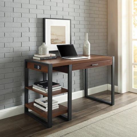 A modern writing desk with a medium brown wood top and frame, black metal legs, and three open side shelves, styled in a home office setting against a gray brick wall.